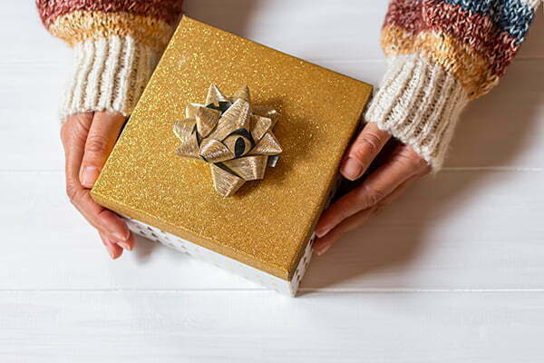 christmas gift hand girl winter warm sweater holds golden box with shiny bow